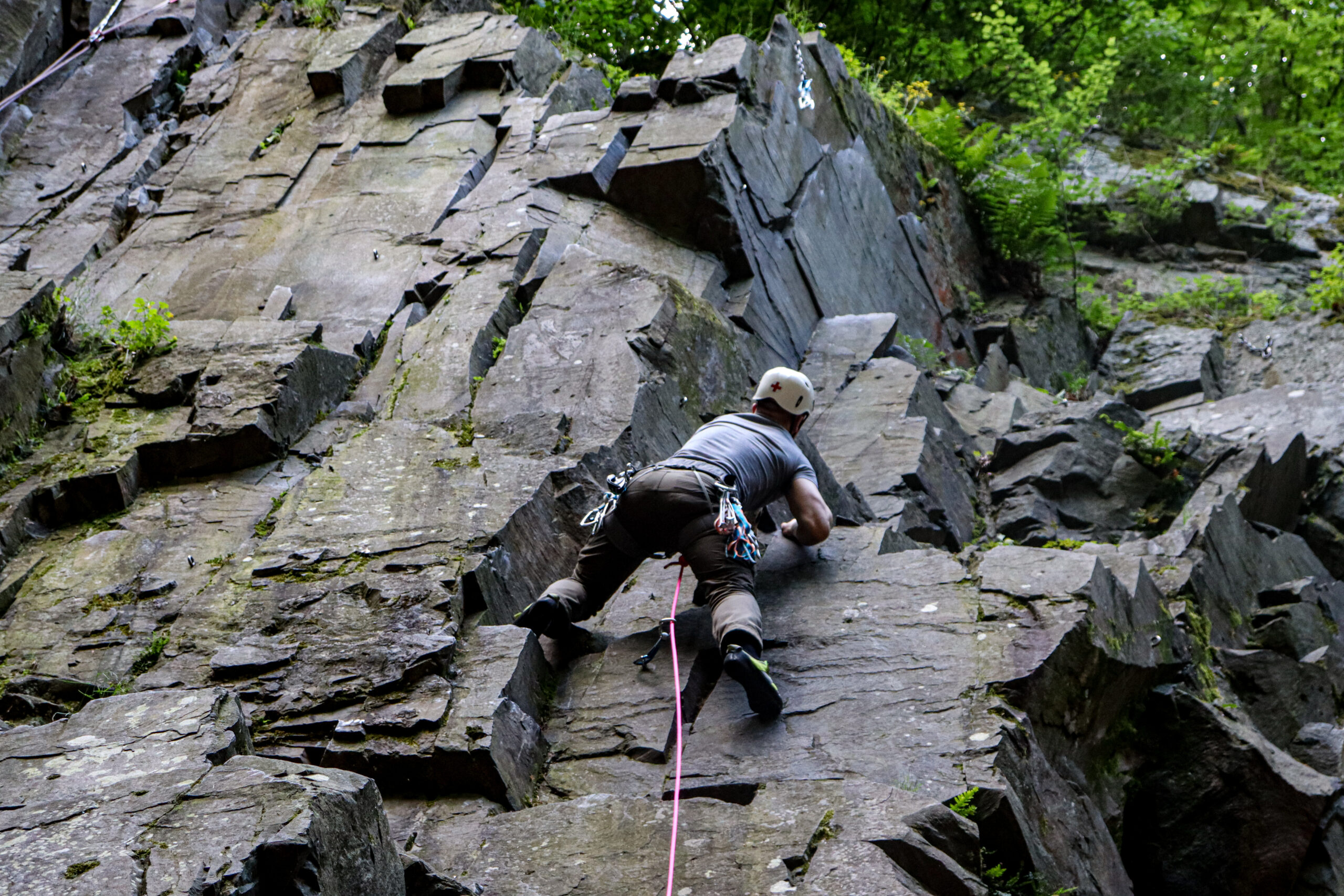 Climber ascending a rock face beside green woodland