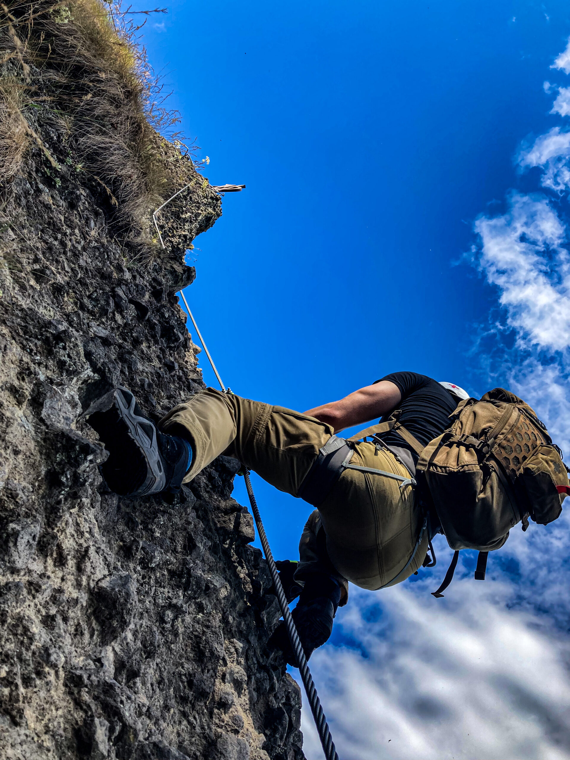 Climber on a via ferrata cable beneath a blue sky