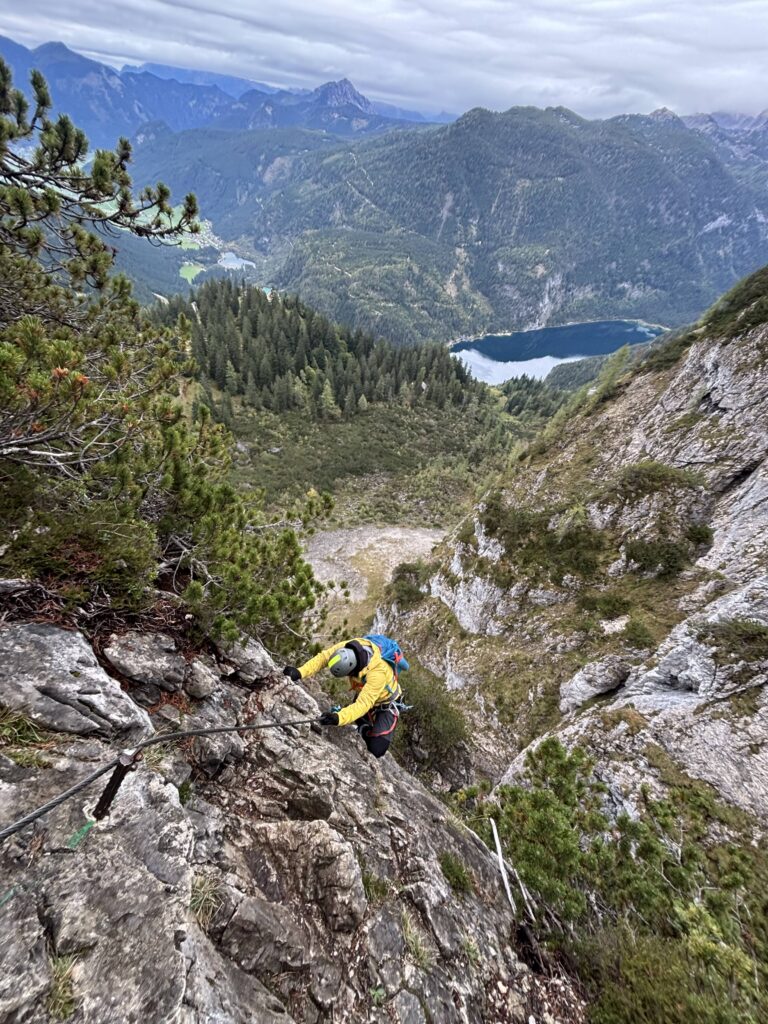 Climber in a yellow jacket on a steep limestone via ferrata, with a lake far below
