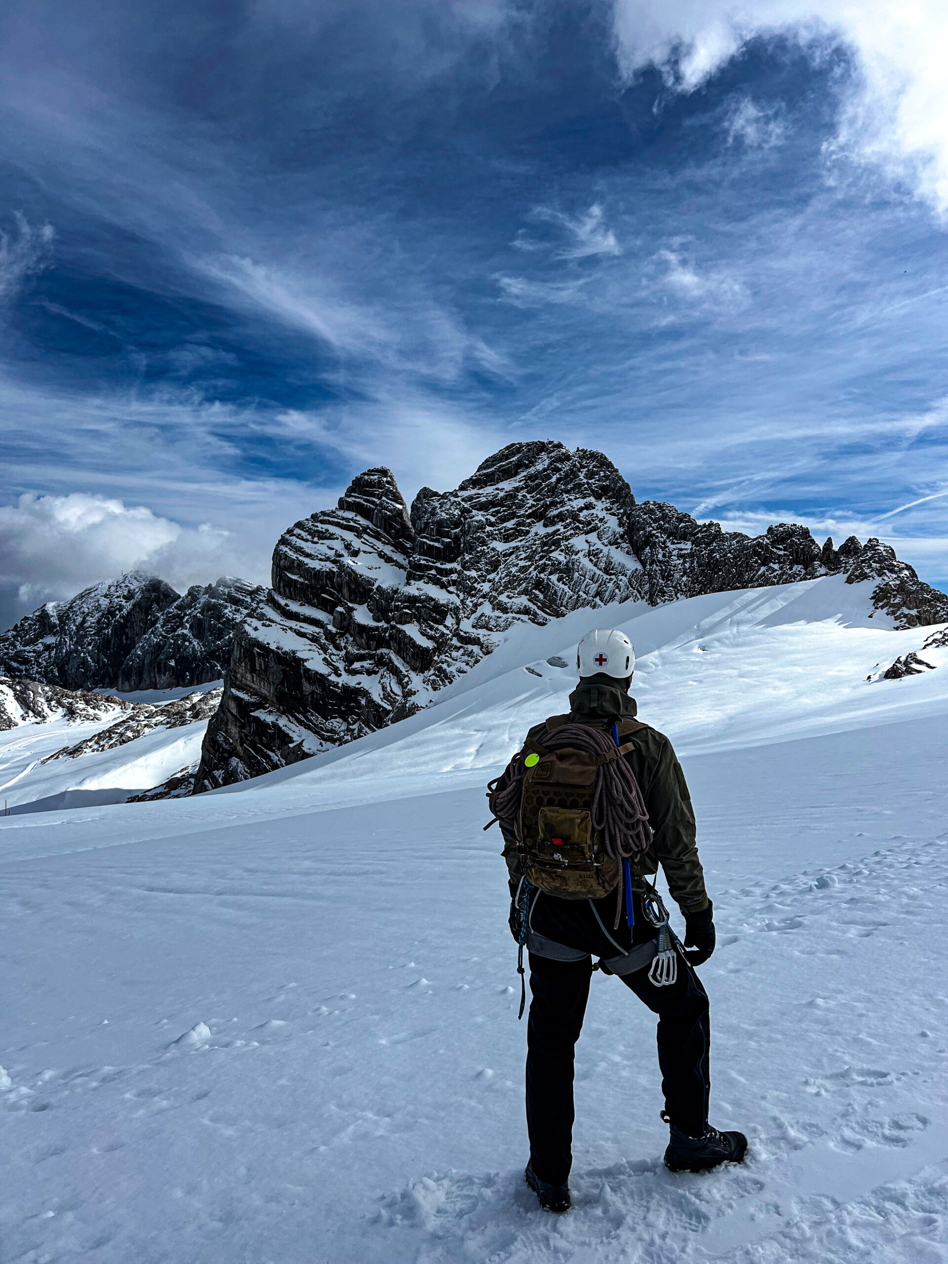 Climber with a rope and backpack facing snow-covered mountains