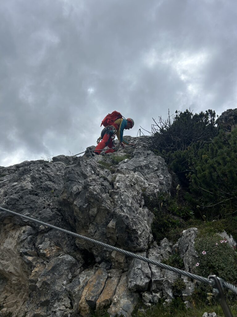 Climber in red trousers following a protected cable route on rocky mountain terrain