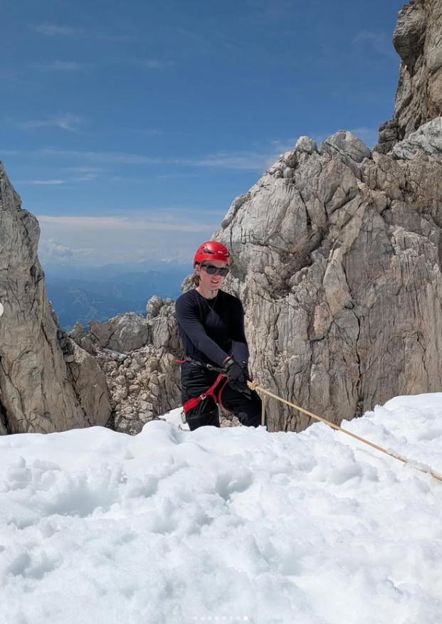 Woman in a red climbing helmet and harness on snow between rocky mountain walls